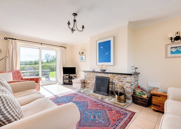A living room with a fireplace, a television, a large window, and a patterned rug. - Tresow (Wadebridge)
