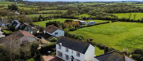 A white house with a tiled roof, surrounded by green fields and a small body of water.