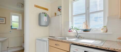 A compact kitchen with a built-in washing machine, a window with a view, and a small window sill with decorative items.
