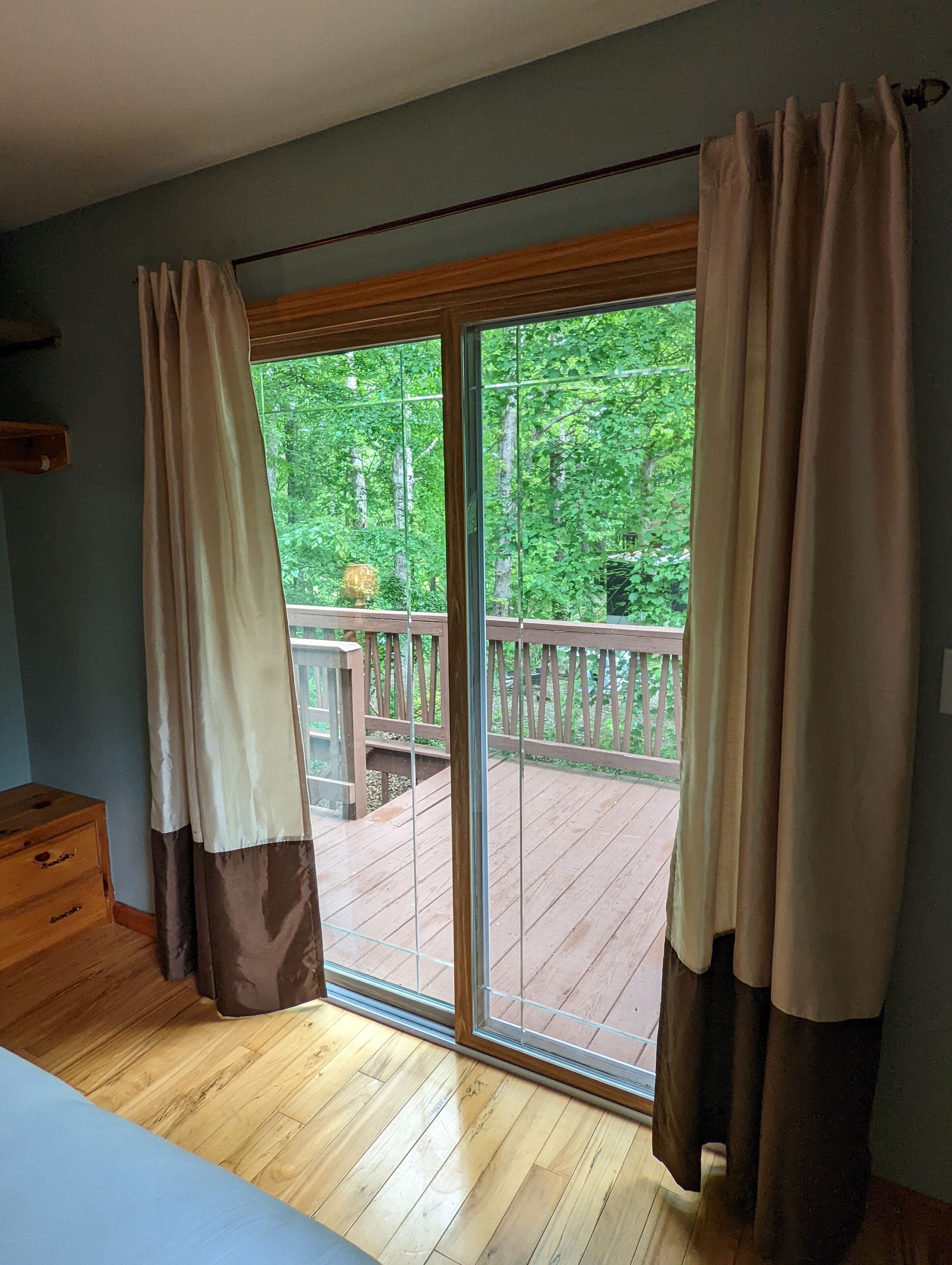 A room with a wooden floor, a sliding glass door leading to a deck, and a wooden dresser.