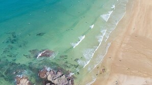 An aerial view of a beach with clear turquoise water, a sandy shore, and rocky outcrops.