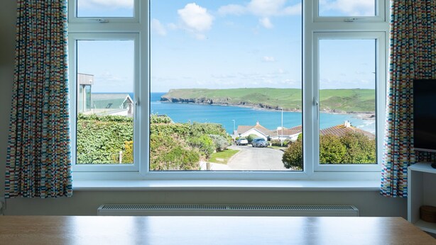 A room with a large window offering a coastal view, including a road and buildings.