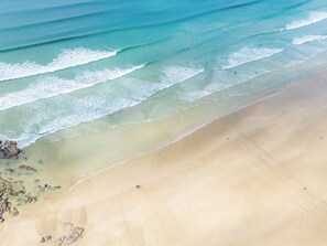 A beach with clear turquoise water, gentle waves, and a wide sandy shore. - Windyhill (Wadebridge)