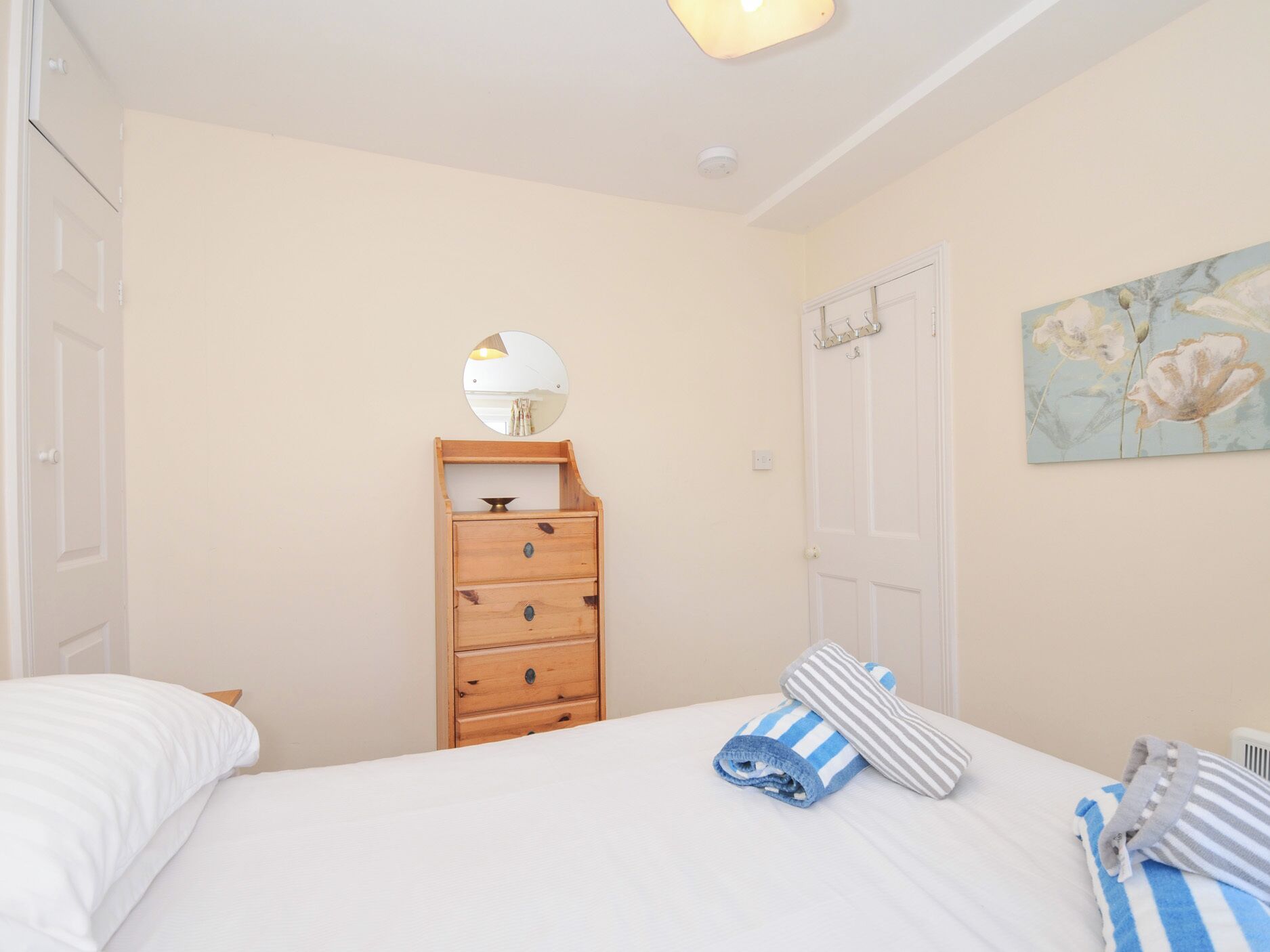 A bedroom with a bed, a wooden dresser with drawers, a mirror, and a painting on the wall.