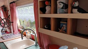 Une cuisine avec un évier, une fenêtre ornée de rideaux en dentelle et des étagères décorées de divers objets.