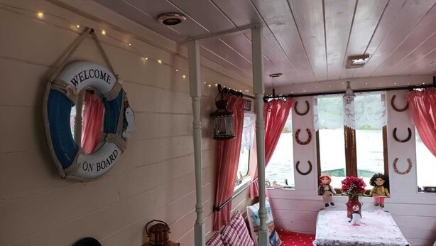 L’intérieur d’un chalet accueillant, avec un plafond en bois, une bouée accrochée au mur, une table recouverte d’une nappe blanche et une vue sur l’eau à l’extérieur.