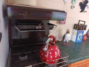 A kitchen with a REVUE Plus oven, a red kettle on the stove, and a bird-shaped decoration on the counter. - Pretty & Cosy Boat in Stunning Valley View, Wales (Rhayader)