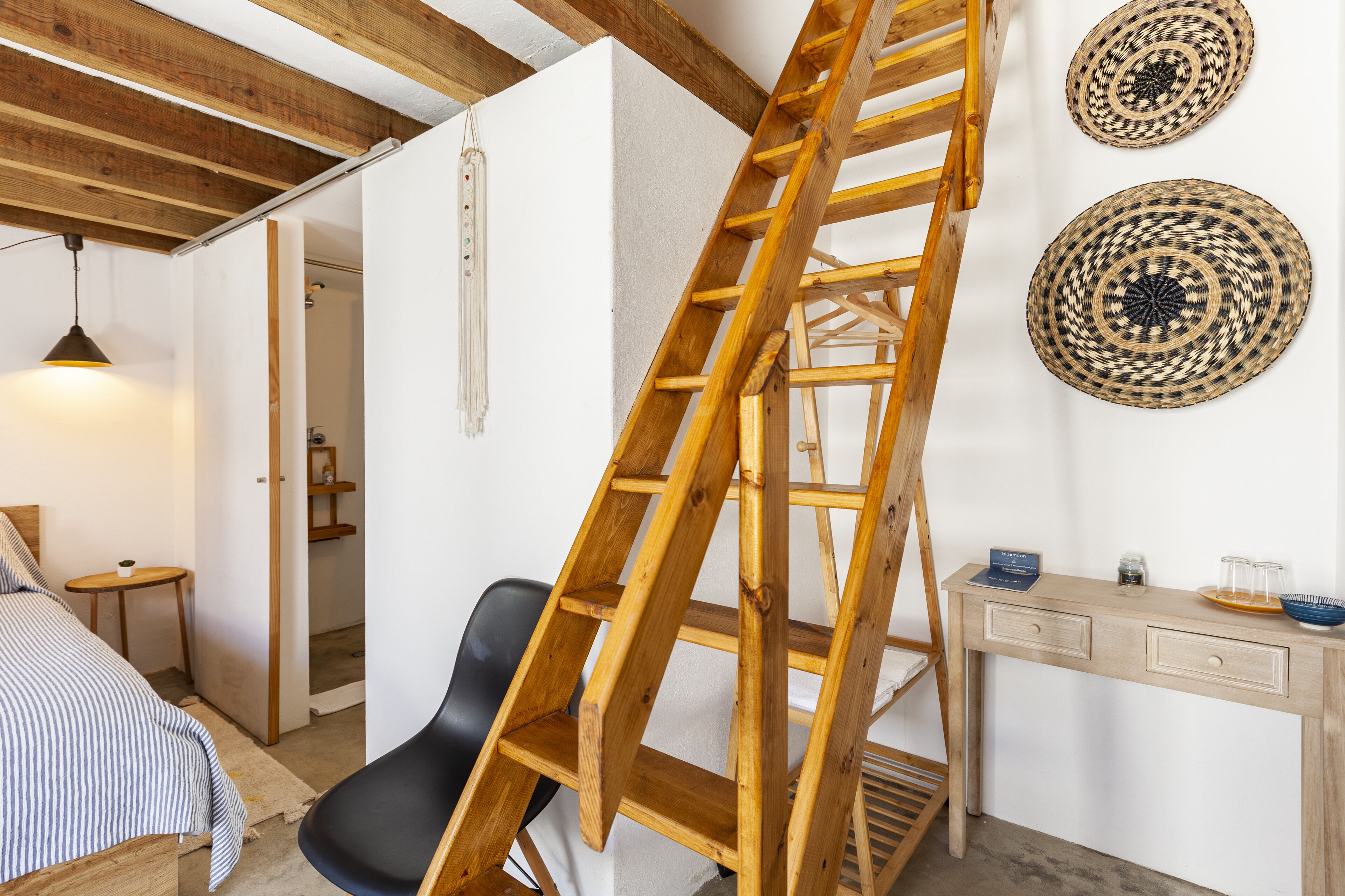 Una habitación con una escalera de madera, un escritorio con un bol y vasos, y dos adornos tejidos en la pared.
