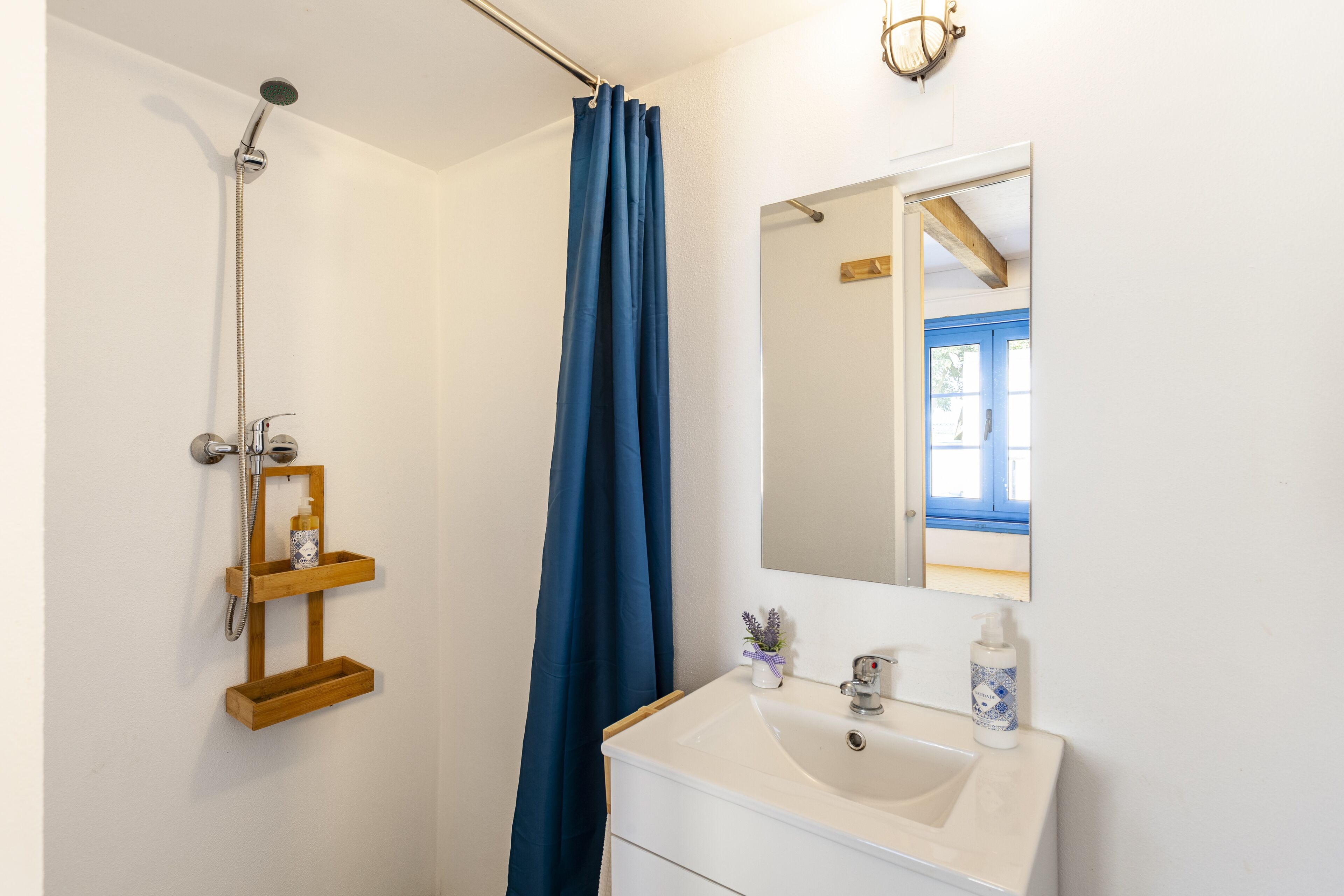 Een badkamer met een douche, wastafel, spiegel en een blauw douchegordijn.