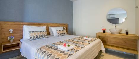 A hotel room with a wooden headboard, a large bed with patterned bedding, a bedside table with a lamp, a wooden dresser with a mirror, and a bathroom with a sink and a toilet.