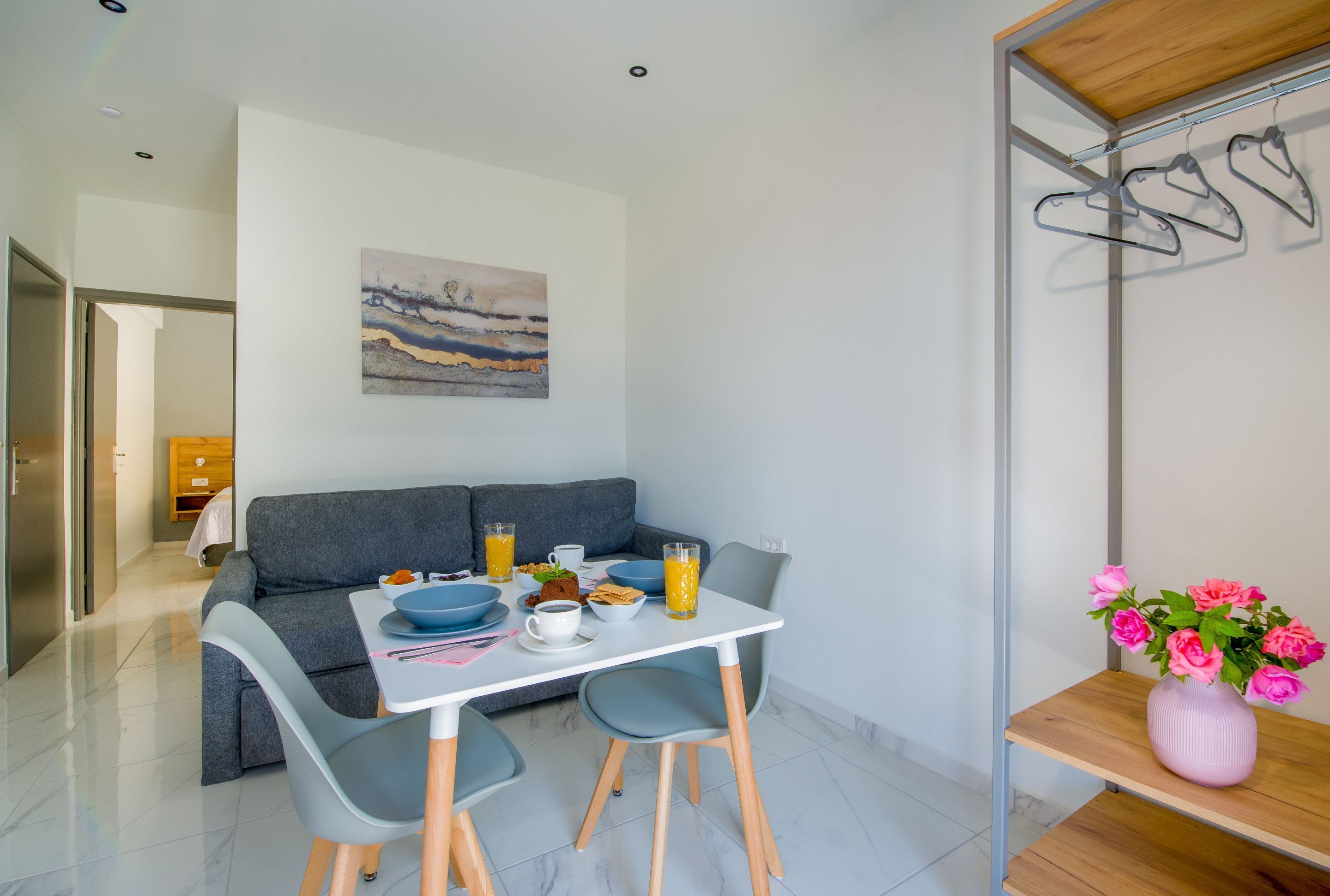 Una sala de estar moderna con comedor, sofá gris, mesa blanca y un cuadro en la pared.