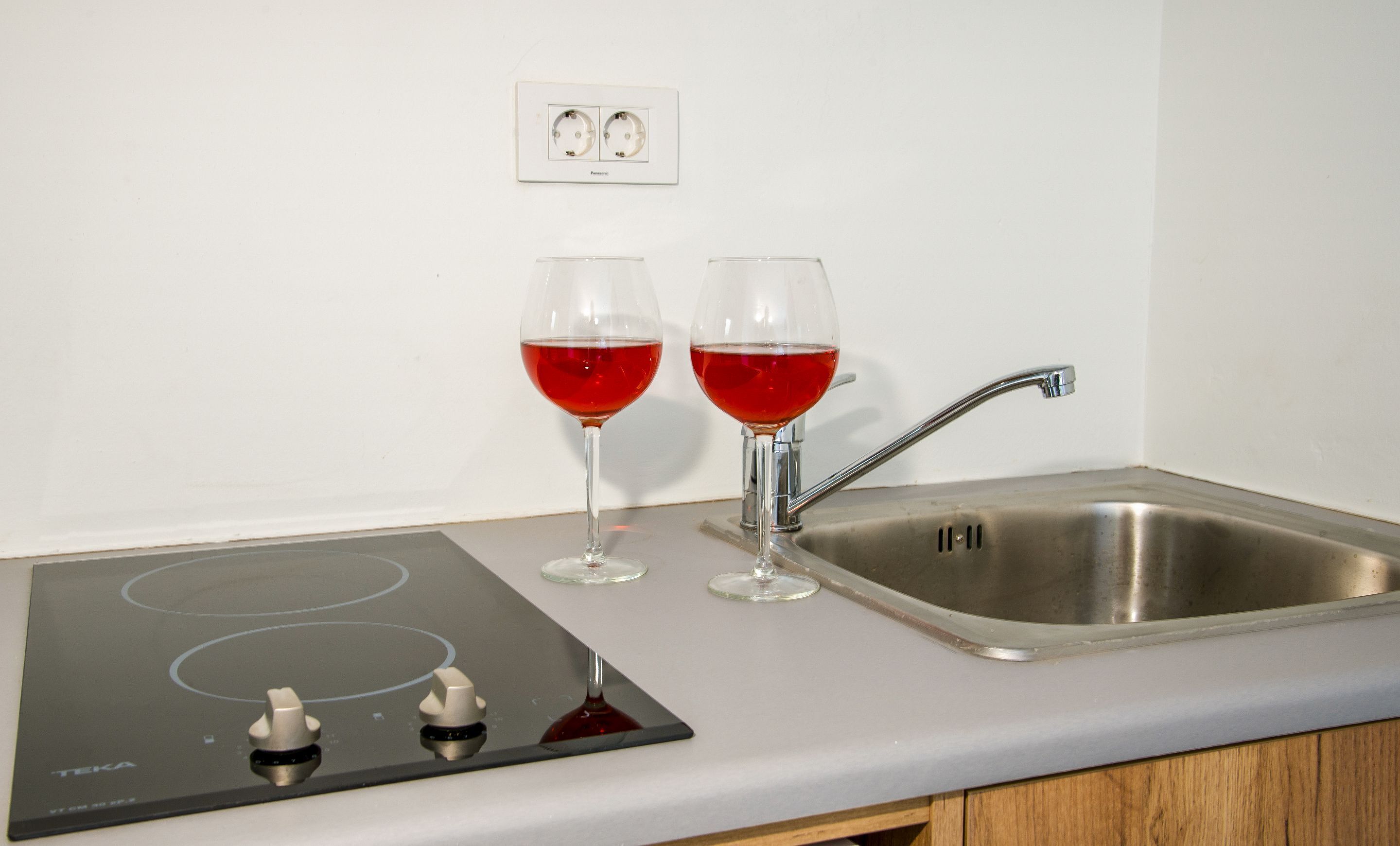 A kitchen with a built-in induction cooktop, a stainless steel sink, and two glasses of red liquid.
