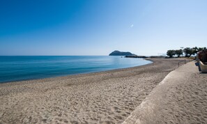 Une plage avec une promenade en béton, un petit bâtiment et une île qui se dessine à l’horizon.