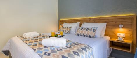 A neatly made bed with a patterned bedspread, two pillows, a bedside table with a cup and a light, and a tray with a towel and orange juice.