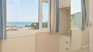 Une pièce dotée d’une grande fenêtre donnant sur la mer et les bâtiments, d’un radiateur blanc et d’un meuble blanc avec des tiroirs.