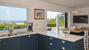 Une cuisine moderne dotée d’une grande fenêtre, d’une machine à café et d’un coin repas offrant une vue sur la mer.
