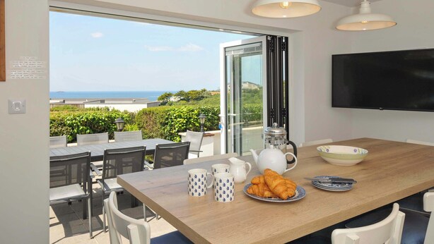 Un espace repas moderne avec une table en bois, des chaises et une vue sur la mer.
