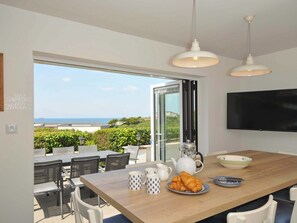 Un espace repas moderne avec une table en bois, des chaises et une vue sur la mer.