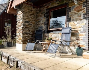 A stone building with a patio area featuring two lounge chairs and a small table.
