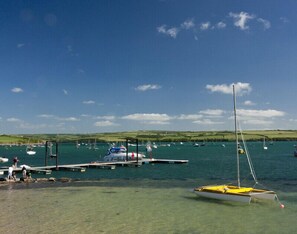 A marina with boats docked, clear water, and a hilly landscape in the background. - Alpine Lodge (Wadebridge)