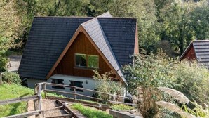 Eine kleine Holzhütte mit Dreiecksdach, umgeben von üppigem Grün und blauem Himmel.