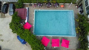 Piscina retangular com deck ladrilhado, rodeada por vegetação e mobiliário de exterior.