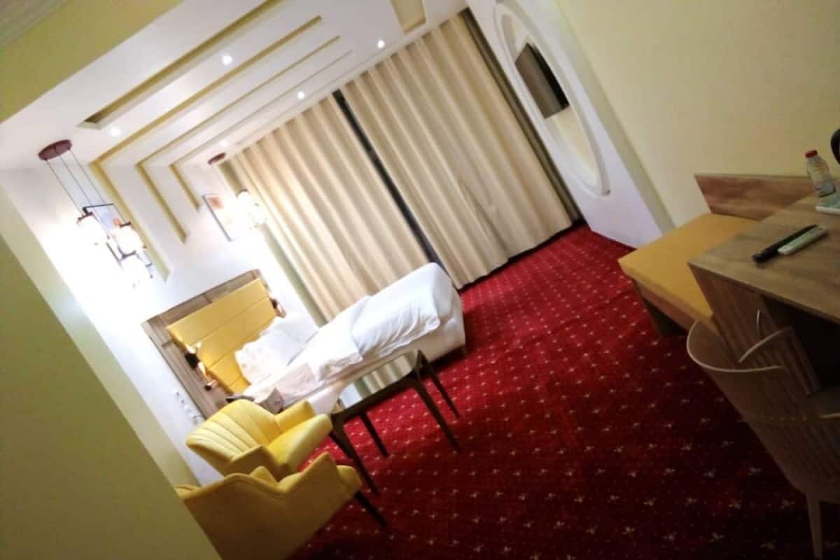 Een hotelkamer met een bed, een bureau, een stoel en een roodgekleurd tapijt.