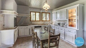 A kitchen with white cabinets, a dining table with chairs, a built-in oven, and a window with a view of trees.