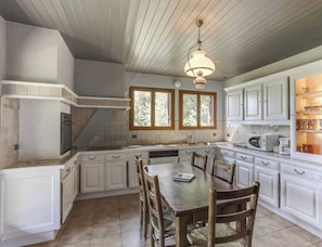 A kitchen with white cabinets, a dining table with chairs, a built-in oven, and a window with a view of trees. - Bergerie – Loft Apartment with Panoramic Lake & Mountain Views (Talloires-Montmin)