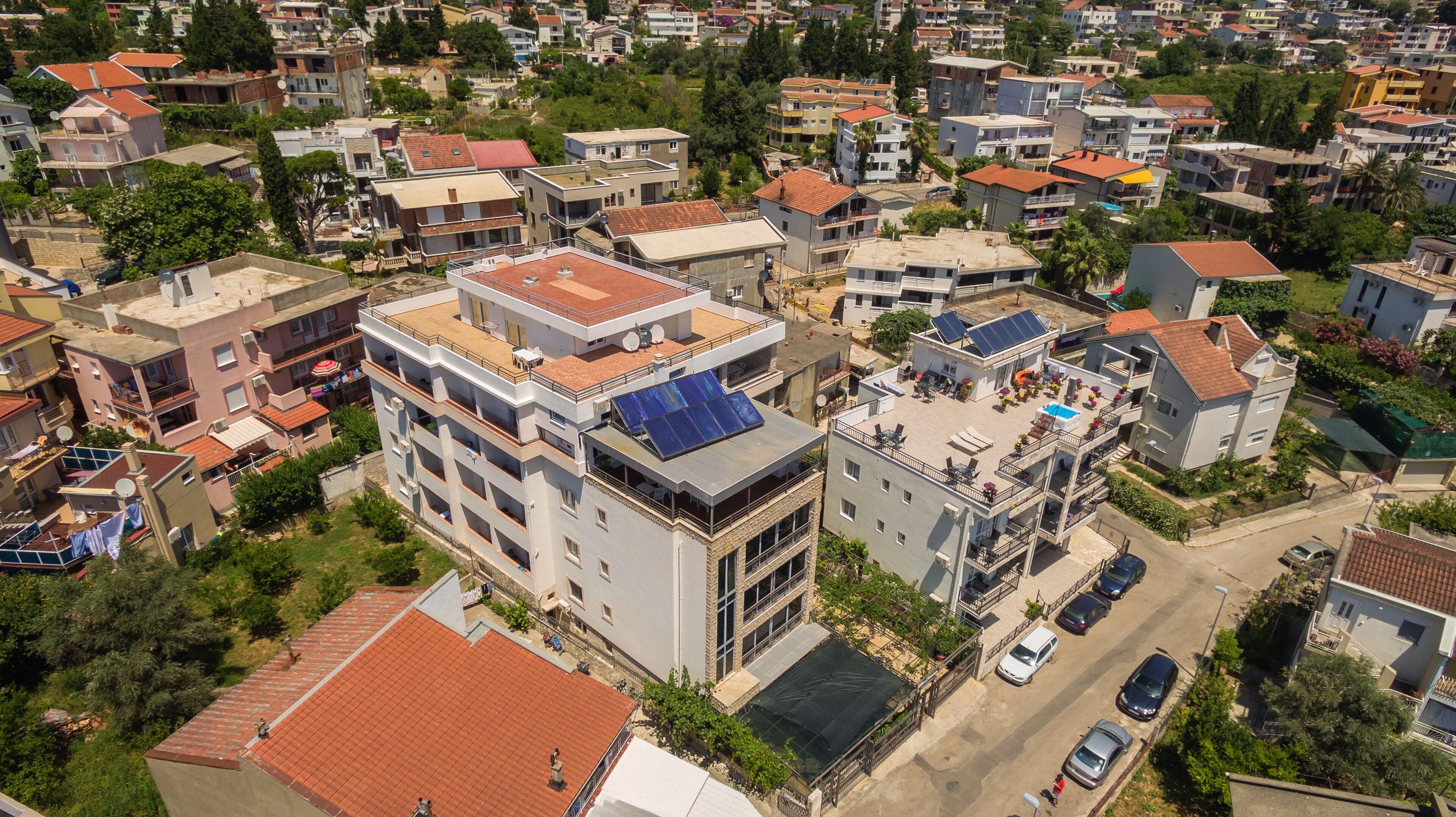 A residential area with multi-story buildings, some with balconies and solar panels, and a street with parked cars.