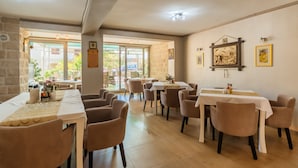 Un restaurante con varias mesas y sillas, una pared de piedra y obras de arte en las paredes.