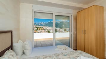 A bedroom with a bed, a wooden wardrobe, and a sliding glass door leading to a balcony with a mountain view.