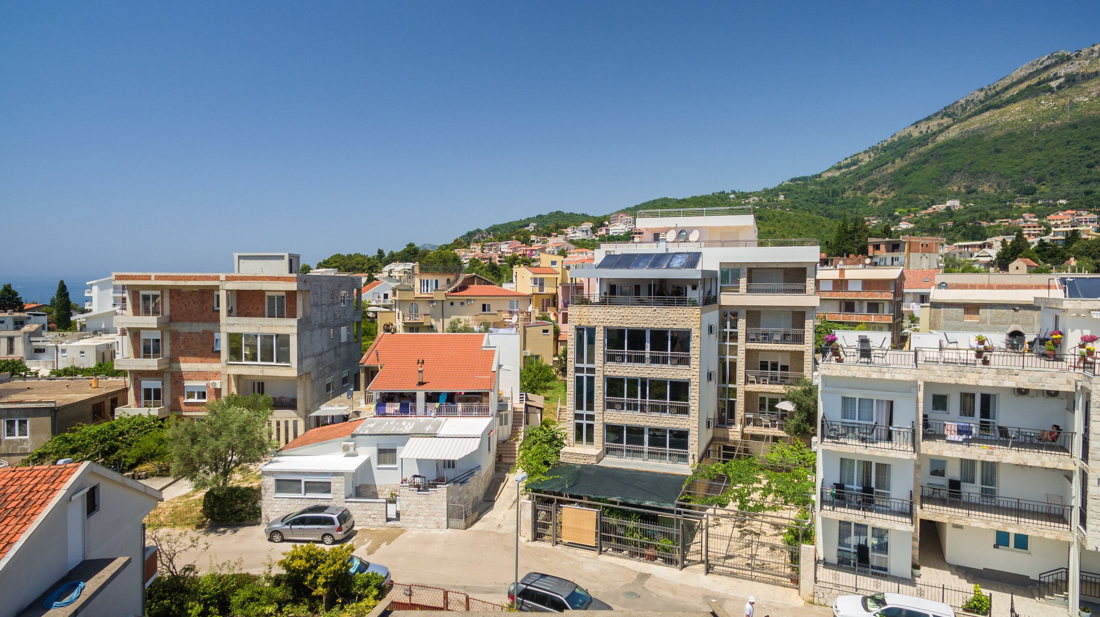 A coastal town with modern multi-story buildings, some with balconies and solar panels, and a clear view of the sea.