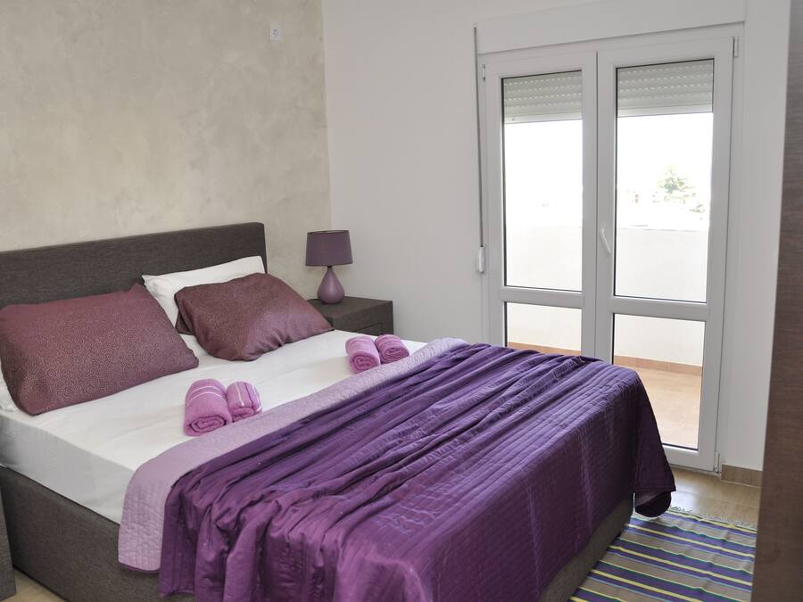 A bedroom with a bed, pillows, a nightstand, a lamp, and a view through a sliding door.