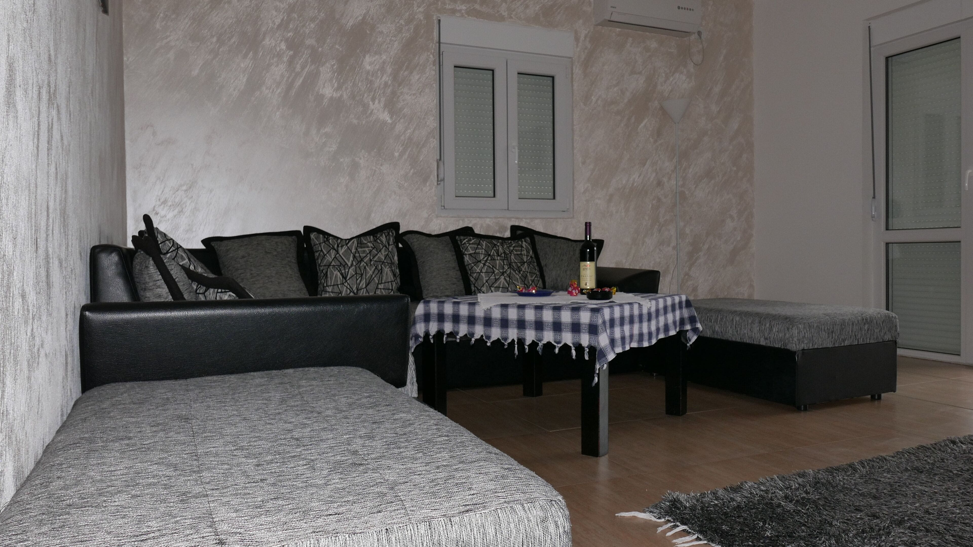 En moderne stue med en sort lædersofa, et matchende skammel og et lille bord med et ternet dug.