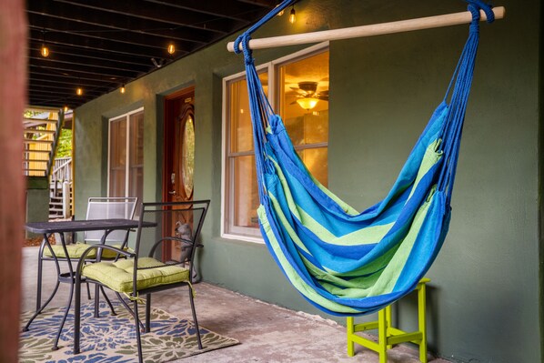A hammock hanging from a wooden beam, a table with chairs, and a window with a view of a staircase. - Romantic Getaway at Chimney Rock + Lake Lure (Chimney Rock)