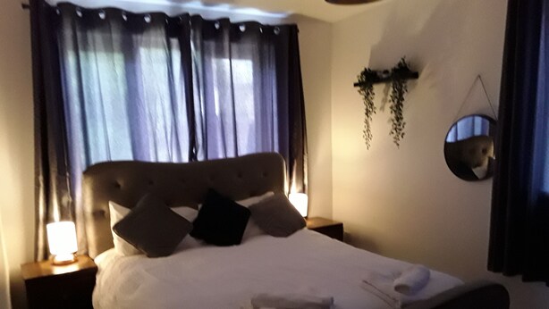 Un lit bien fait, avec des oreillers et une couverture, une lampe de chevet, un miroir fixé au mur et une plante suspendue.