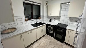 Une cuisine moderne avec des meubles blancs, un évier noir, un lave-linge encastré et une cuisinière.