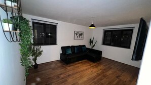 Un salon avec un canapé noir, un plancher en bois, une plante suspendue et une carte du monde accrochée au mur.