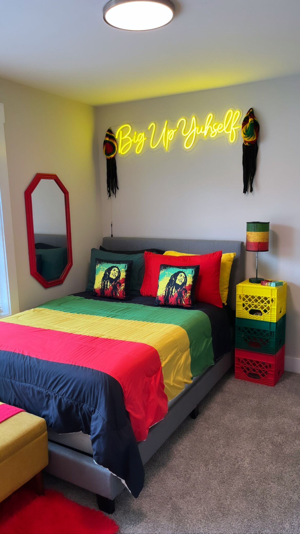 Ein Schlafzimmer mit einem Bett, farbenfrohen Kissen, einer Neonreklame, einem Spiegel und einer Lampe auf einer Kiste.
