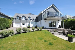 A two-story house with a covered patio, a lawn, and potted plants.
