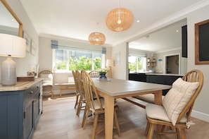 A dining area with a wooden table and chairs, pendant lights, and a view of greenery outside.