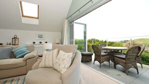 Un salon moderne avec un canapé, une table à manger et des chaises, une grande fenêtre et une vue sur la verdure.
