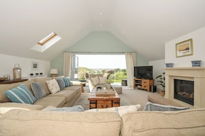 A spacious living area with a high ceiling, a sofa set, a television, and a fireplace.