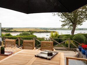 A wooden deck with a table set for dining, overlooking a river with boats. - Little Strand (Wadebridge)