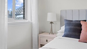 Un dormitorio con una cama, una mesita de noche, una lámpara y un ventanal con vistas a un puente.