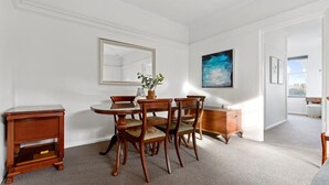 Un comedor con una mesa redonda, cuatro sillas, una mesita de madera, un aparador y un espejo grande en la pared.