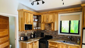Una cocina con armarios de madera, protector contra salpicaduras de piedra, estufa negra, pileta y ventana con vista a follaje.