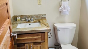 Un baño con lavamanos, inodoro, armarios de madera y encimera de mármol.