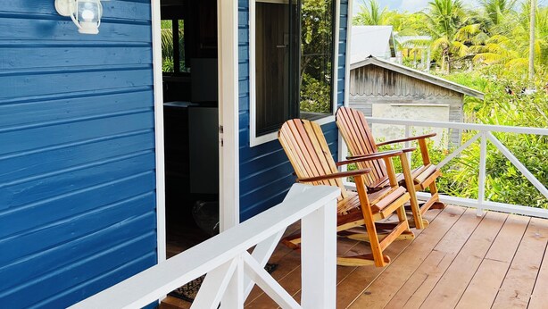 Una casa azul con porche, sillas de madera y baranda blanca.